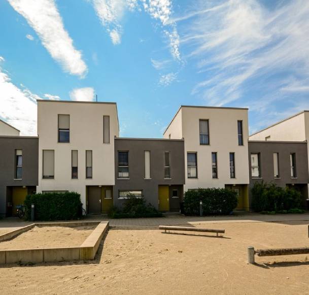 A row of houses on the sand in front of trees.