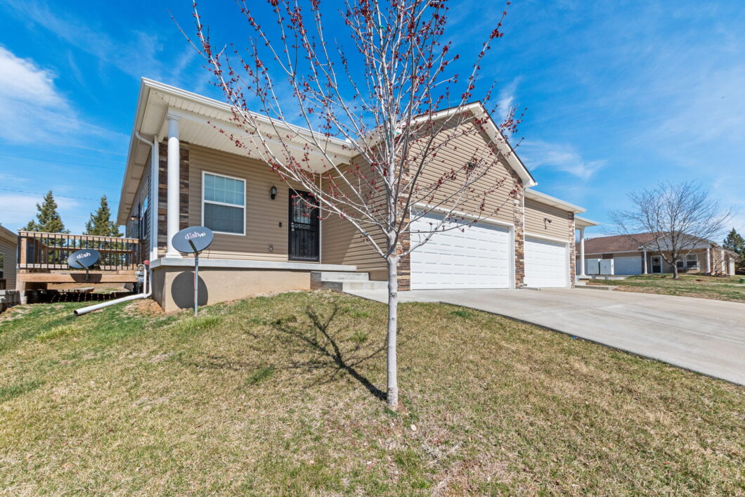 A house with two garage doors and a tree in front of it.