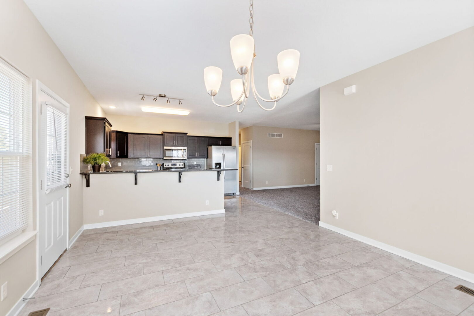 A large open living room with white walls and beige tile flooring.